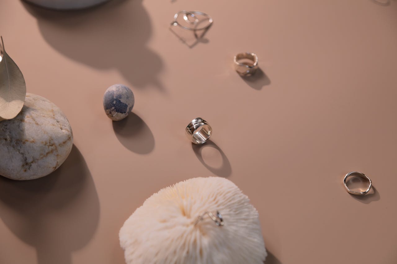 Minimalist arrangement of silver rings on a beige background with stones and a feather.